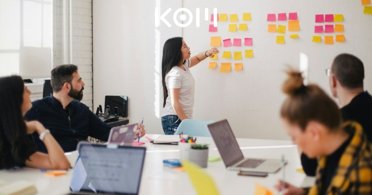 Equipo de agencia de marketing digital KOM Perú colaborando en estrategia de redes sociales: pizarra con post-its, laptops y reunión creativa para el puesto de Community Manager Full Time.