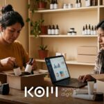 Dos emprendedoras revisan en la laptop los comprobantes electrónicos de su tienda online mientras preparan un pedido y una devolución (comprobantes electrónicos tienda online)